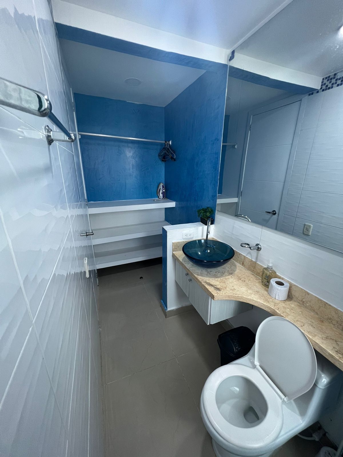 Ein modernes Badezimmer mit blauer Akzentwand, einem weißen Waschbecken mit blauer Schüssel, einer weißen Toilette und einem Spiegel über dem Waschbecken.