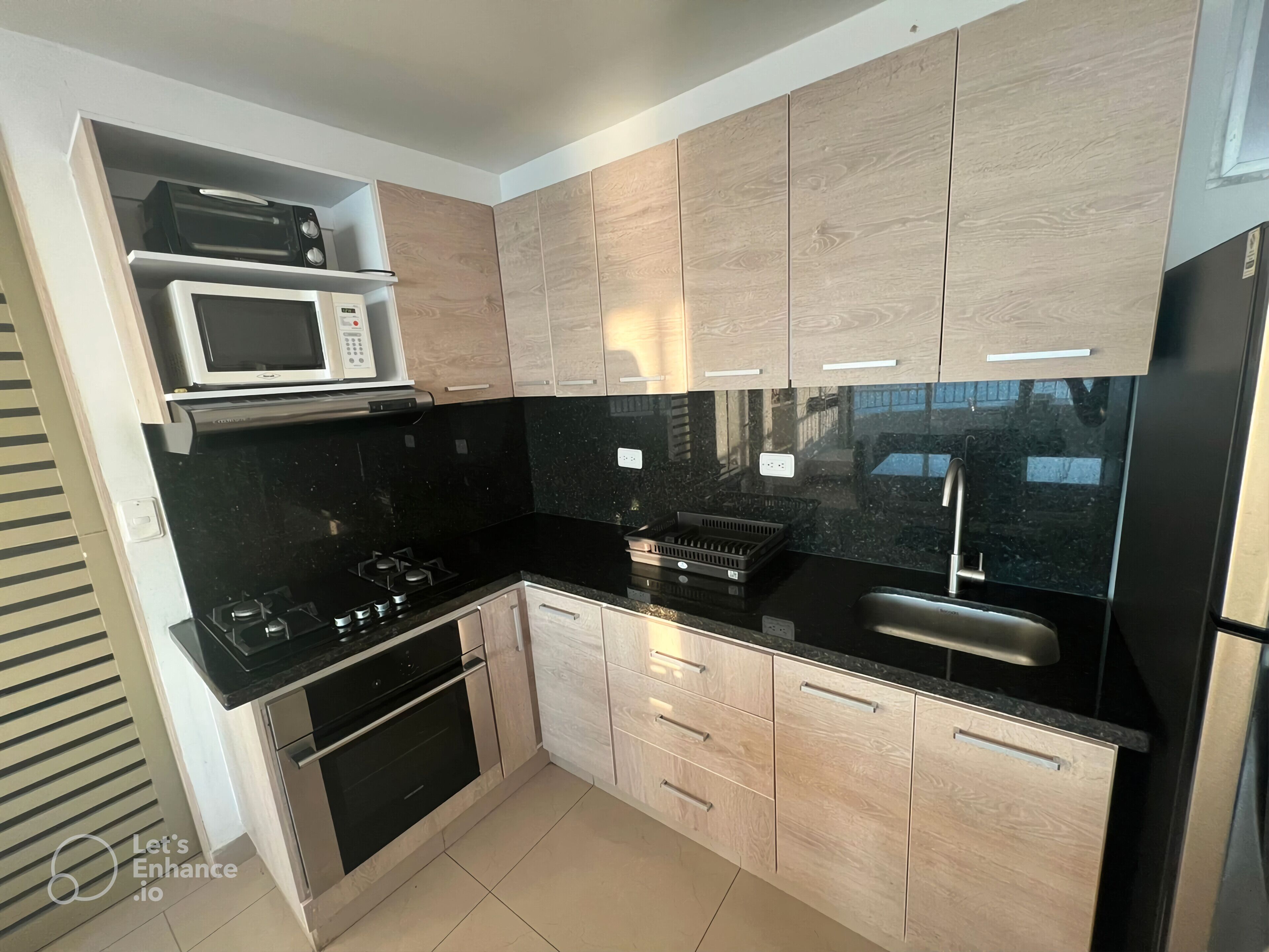 A modern kitchen with black countertops, wooden cabinets, a built-in microwave, a gas stove, and a stainless steel sink.