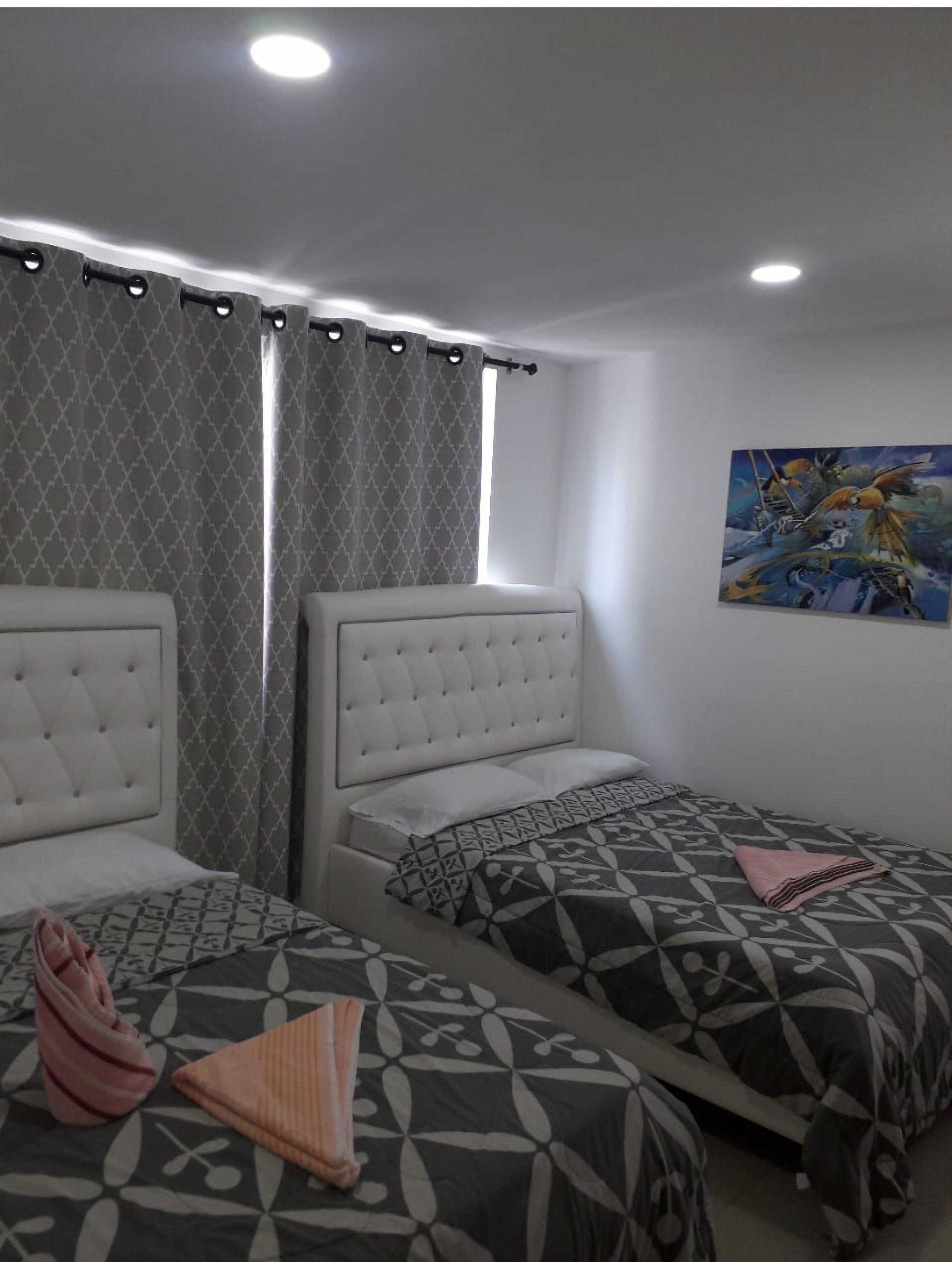 A bedroom with two beds, a window with curtains, and a painting on the wall.