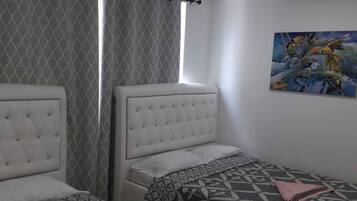 A bedroom with two beds, a window with curtains, and a painting on the wall.