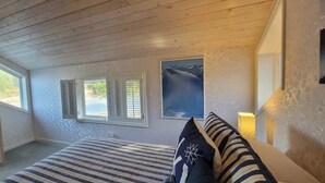 Een slaapkamer met een bed, een dressoir, een raam met luiken en een schilderij aan de muur.