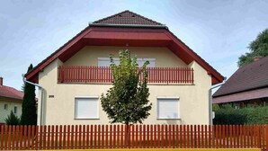 Ein zweistöckiges Haus mit rotem Dach, gelbem Zaun und einem Baum davor.