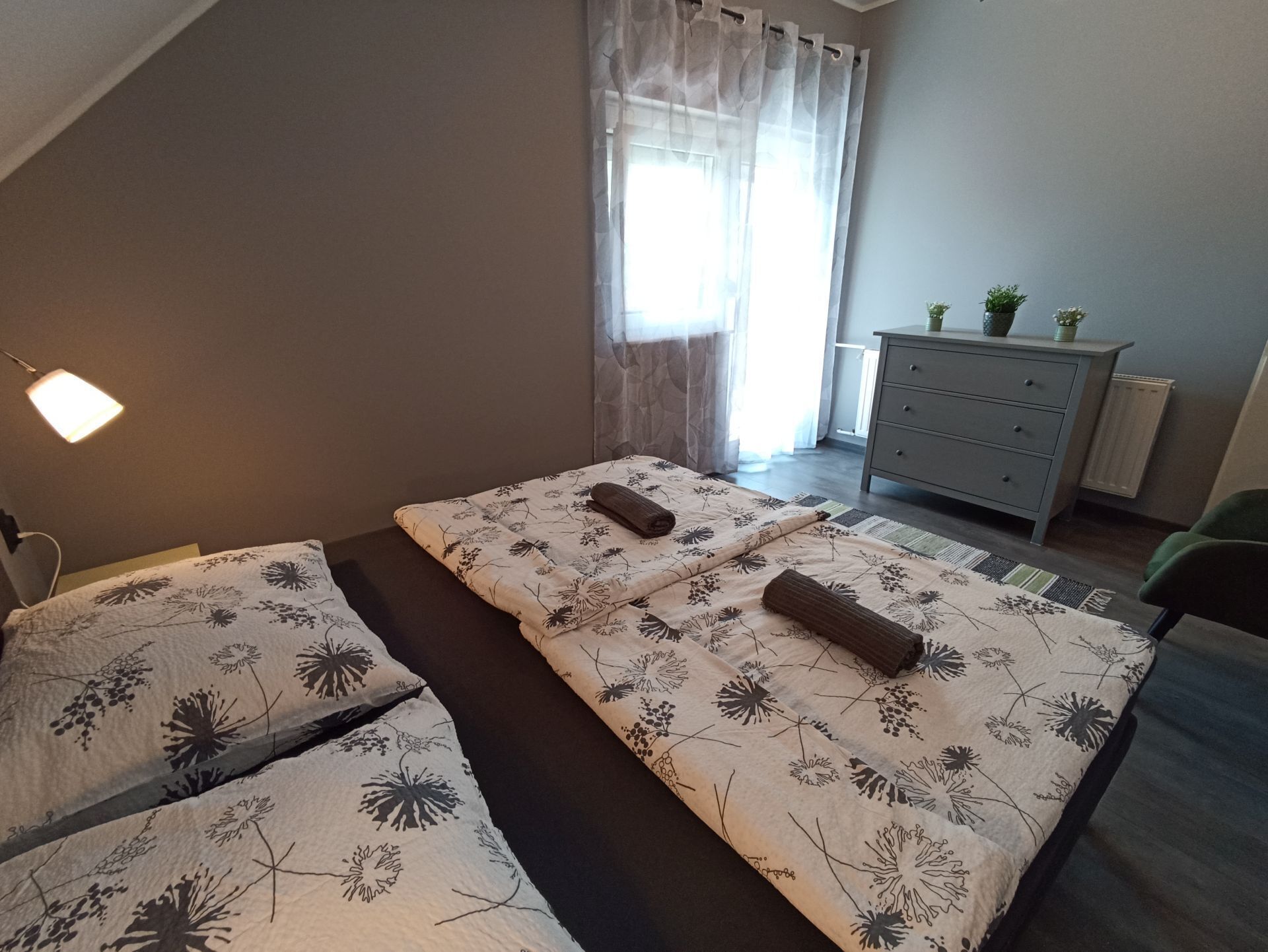 Un dormitorio con una cama, un aparador, una lámpara y una ventana con cortinas.