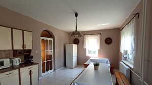 Eine Küche mit Mikrowelle, Wasserkocher und Kaffeemaschine, einem Kühlschrank, einem Esstisch mit einer Bank und einem Fenster mit Vorhängen.