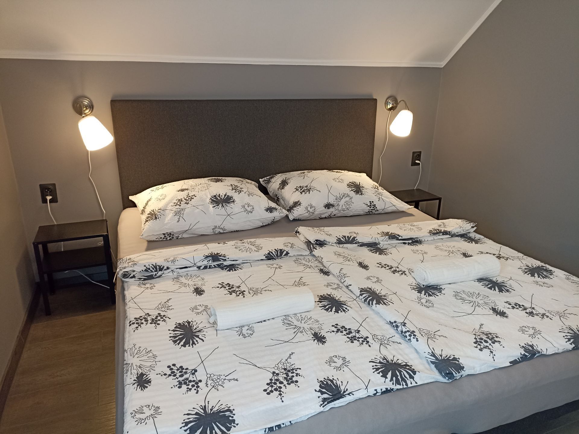 Uma cama bem arrumada com colcha floral, duas luminárias de cabeceira e uma cabeceira.