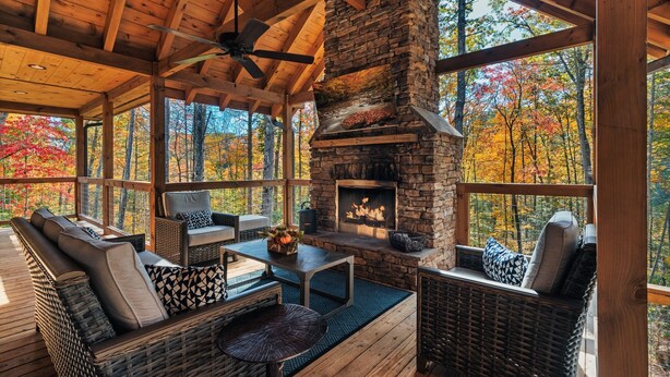 A cozy wooden deck with wicker furniture and a stone fireplace. - LUXURY • Indoor Pool • Firepit • Suround sound Theater • Arcade • Sleeps 12 (Sevierville)