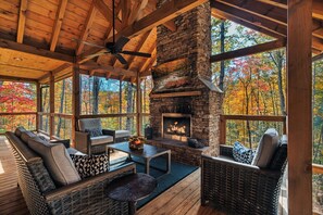 A cozy wooden deck with wicker furniture and a stone fireplace. - LUXURY • Indoor Pool • Firepit • Suround sound Theater • Arcade • Sleeps 12 (Sevierville)