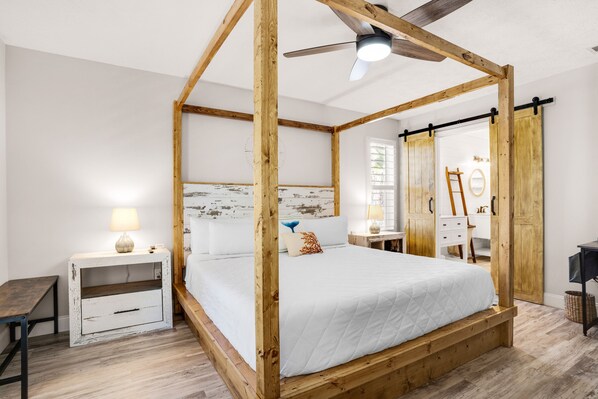 Quarto com cama de dossel, vigas de madeira, ventilador de teto e mesa de cabeceira com abajur.