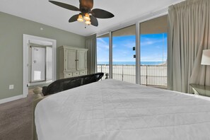 Ein Schlafzimmer mit einem großen Bett, einem Deckenventilator, Blick auf den Ozean und einer Glastür zum Balkon.