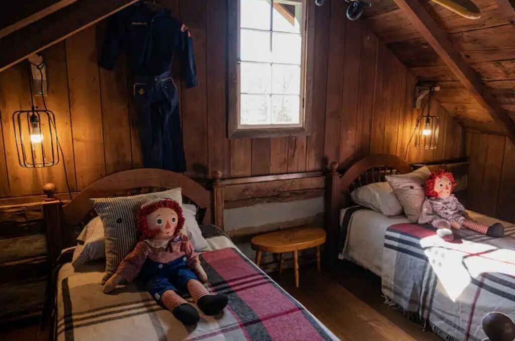 A cozy attic bedroom with two beds, wooden walls, and a window.