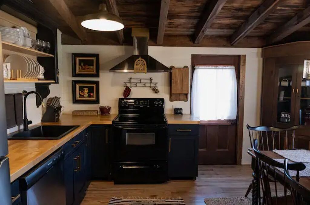 Una cocina con armarios de madera, una estufa negra y un colgador para ollas.