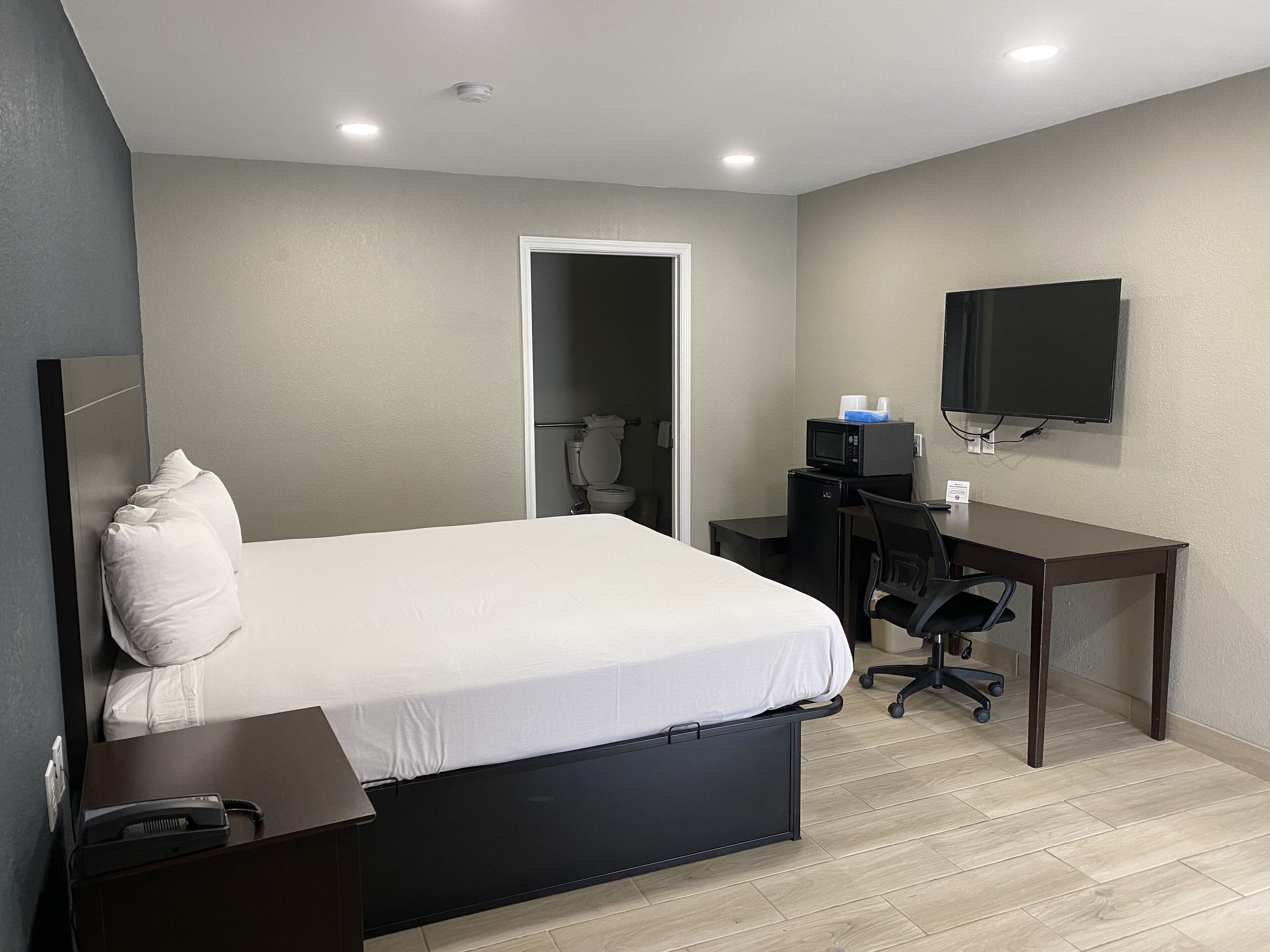 A hotel room with a bed, desk, chair, and a TV mounted on the wall.