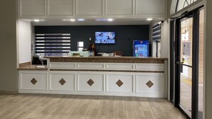 Una cocina con encimera de granito, armarios blancos, ventilador de techo, televisor y refrigerador.