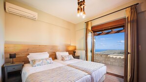 Ein Schlafzimmer mit zwei Betten, einem Nachttisch, einer Klimaanlage, einer Lampe und Meerblick durch eine offene Tür.