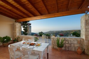 An outdoor dining area with a stone wall and wooden ceiling, overlooking a mountainous landscape. - Villa with private pool & sea view for absolute privacy and serenity. (Rethymno)