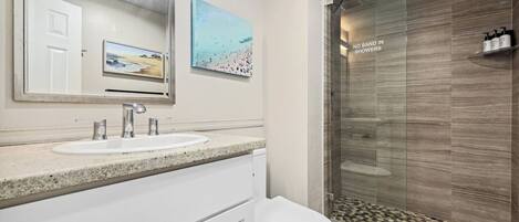 A bathroom with a sink, mirror, toilet, and a glass shower enclosure.