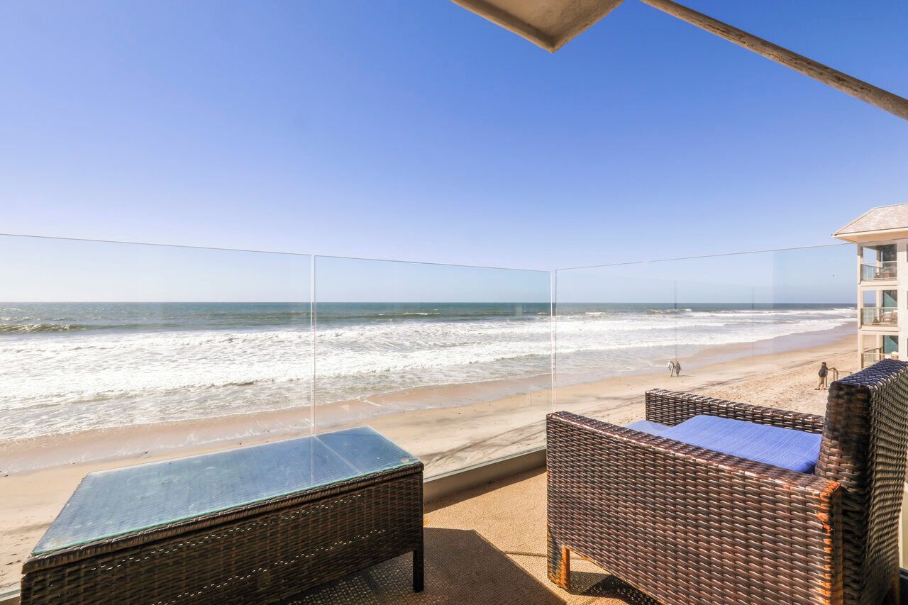 A balcony with wicker furniture overlooking a beach.