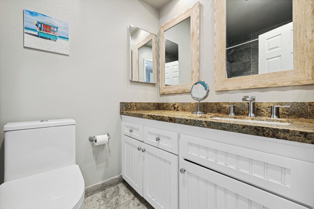 A bathroom with a toilet, a sink with a granite countertop, and two mirrors with wooden frames.