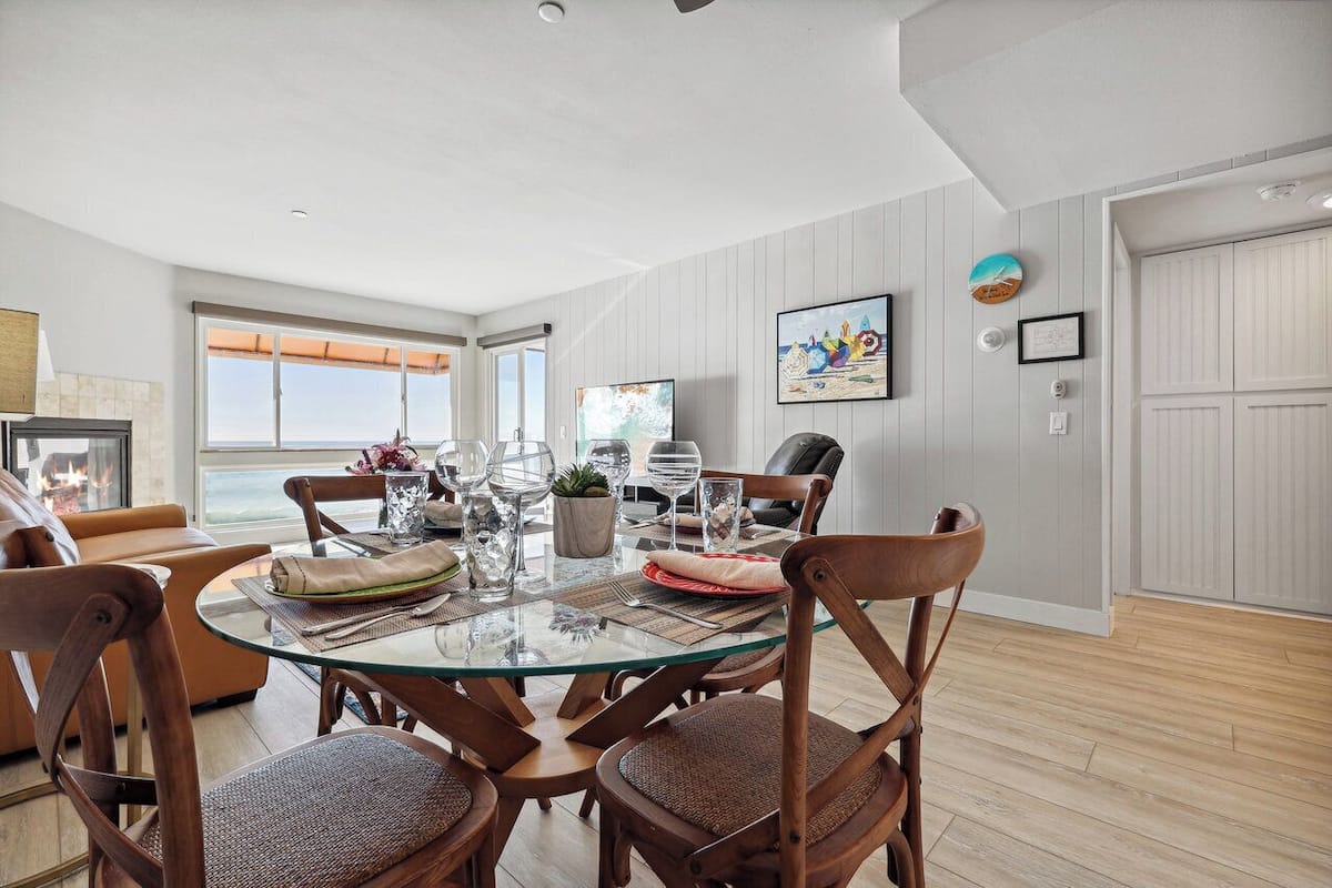 Comedor con mesa de vidrio, sillas de madera y vista al océano.