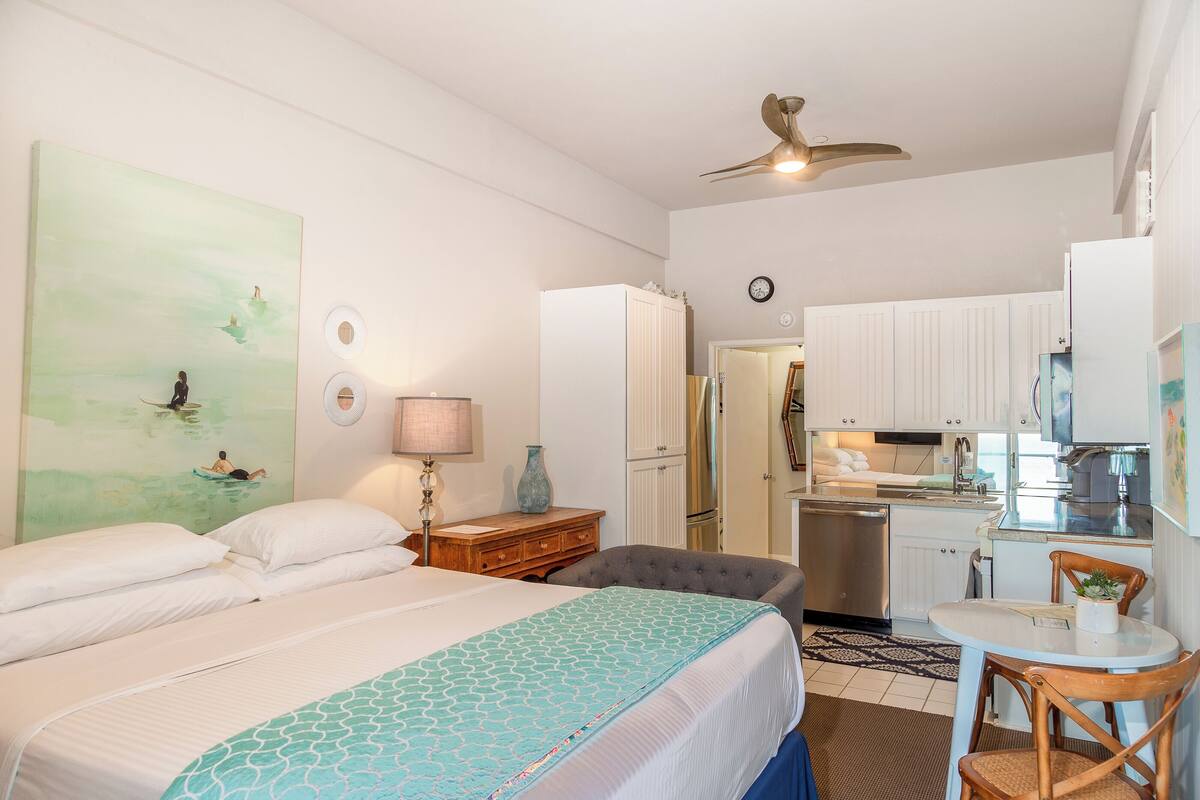 Habitación de hotel con cama, escritorio, silla, kitchenette y baño.