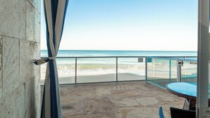 Un balcon doté d’un sol en pierre, d’une rambarde en verre et offrant une vue sur la plage.