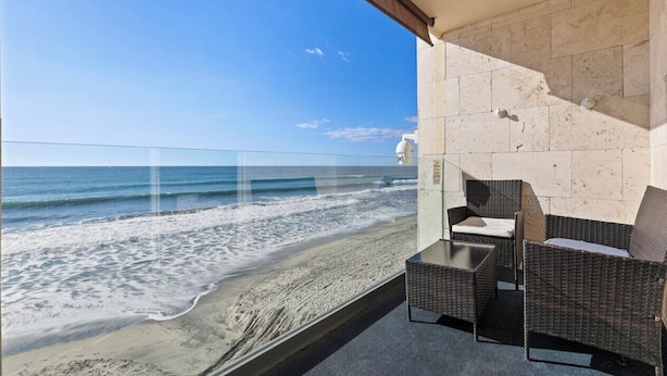 Un balcon meublé avec des meubles en osier, donnant sur une plage.