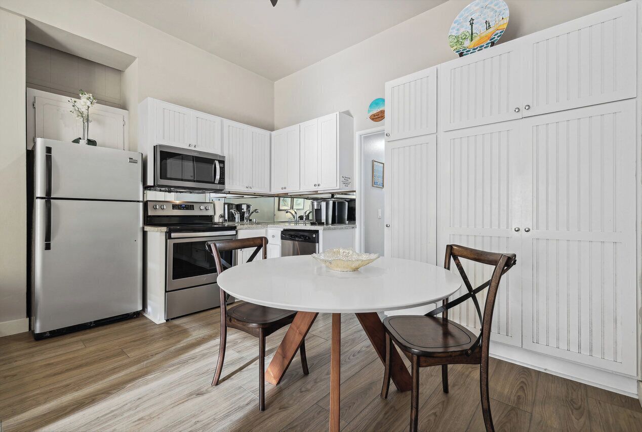 A modern kitchen with white cabinetry, stainless steel appliances, and a round dining table with wooden chairs.