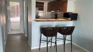 Una cucina moderna con un piano di lavoro, forno integrato e forno a microonde. Sono presenti due sgabelli neri e una finestra con persiane.