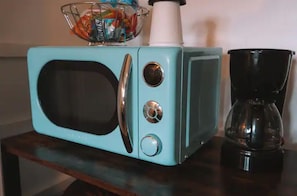 Un four à micro-ondes de couleur turquoise est posé sur une table en bois, à côté d’une machine à café.