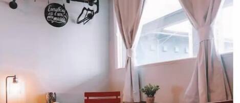 A small room with a bed, a desk, a chair, a table, and a window with curtains.