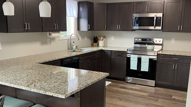 A modern kitchen with dark wood cabinets, stainless steel appliances, and a granite countertop.