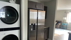 A modern kitchen with a stainless steel refrigerator, a built-in washer and dryer, and a wooden floor.