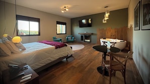 A modern bedroom with a large bed, a fireplace, a dining area, and a TV mounted on the wall.
