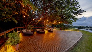 A wooden deck with outdoor seating, surrounded by trees and a view of a body of water.