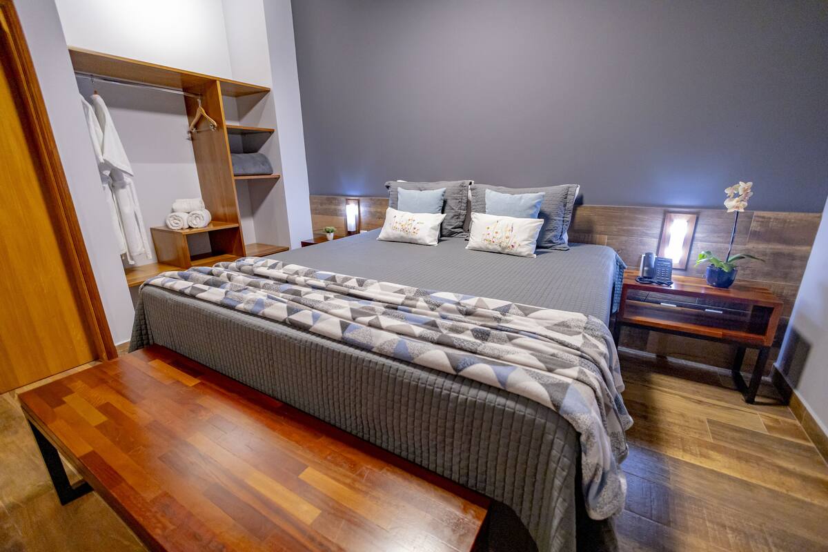 Un dormitorio con cama, mesitas de noche, un banco, un armario y una planta en maceta.