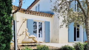 A stone wall, a wooden table with a bottle and glasses, and a house with blue shutters and a tiled roof. - Villa de Charme, à Proximité Immédiate D'uzes et du Pont du Gard (Argilliers)