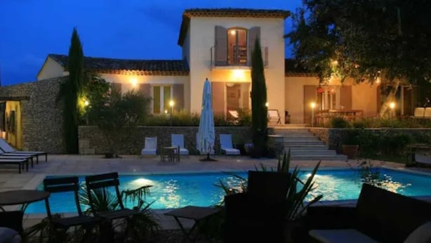 A pool area with lounge chairs and umbrellas, a stone wall, and a building with a balcony. - Villa de Charme, à Proximité Immédiate D'uzes et du Pont du Gard (Argilliers)