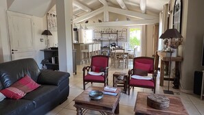 A spacious living room with a black leather sofa, red armchairs, wooden coffee tables, and a dining area with a wooden table and chairs. - Villa de Charme, à Proximité Immédiate D'uzes et du Pont du Gard (Argilliers)