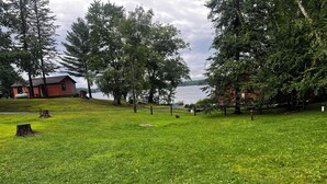 A grassy area with a wooden fence, trees, and a lake in the background. - Birch Point Resort Kitchenette #14 - Lake Nelson, Hayward (Hayward)