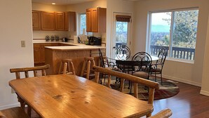 Una cocina amplia con armarios de madera y una isla grande, un comedor con mesa y bancos de madera, y vista a un balcón con barandilla.
