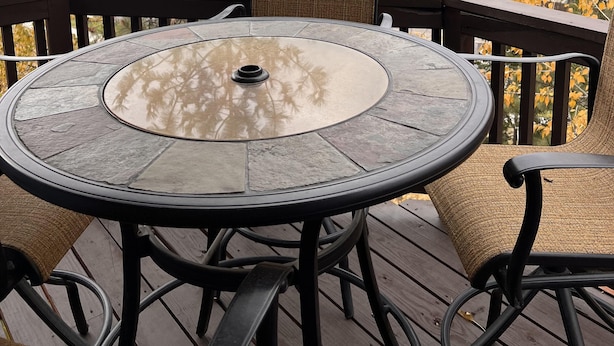 Mesa redonda con sillas en una terraza exterior, con vista a un paisaje montañoso y follaje otoñal.