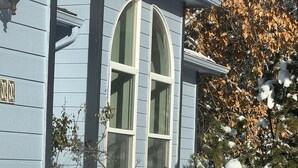 Una casa con un amplio ventanal arqueado, un buzón y un ciervo acostado en la nieve al frente.
