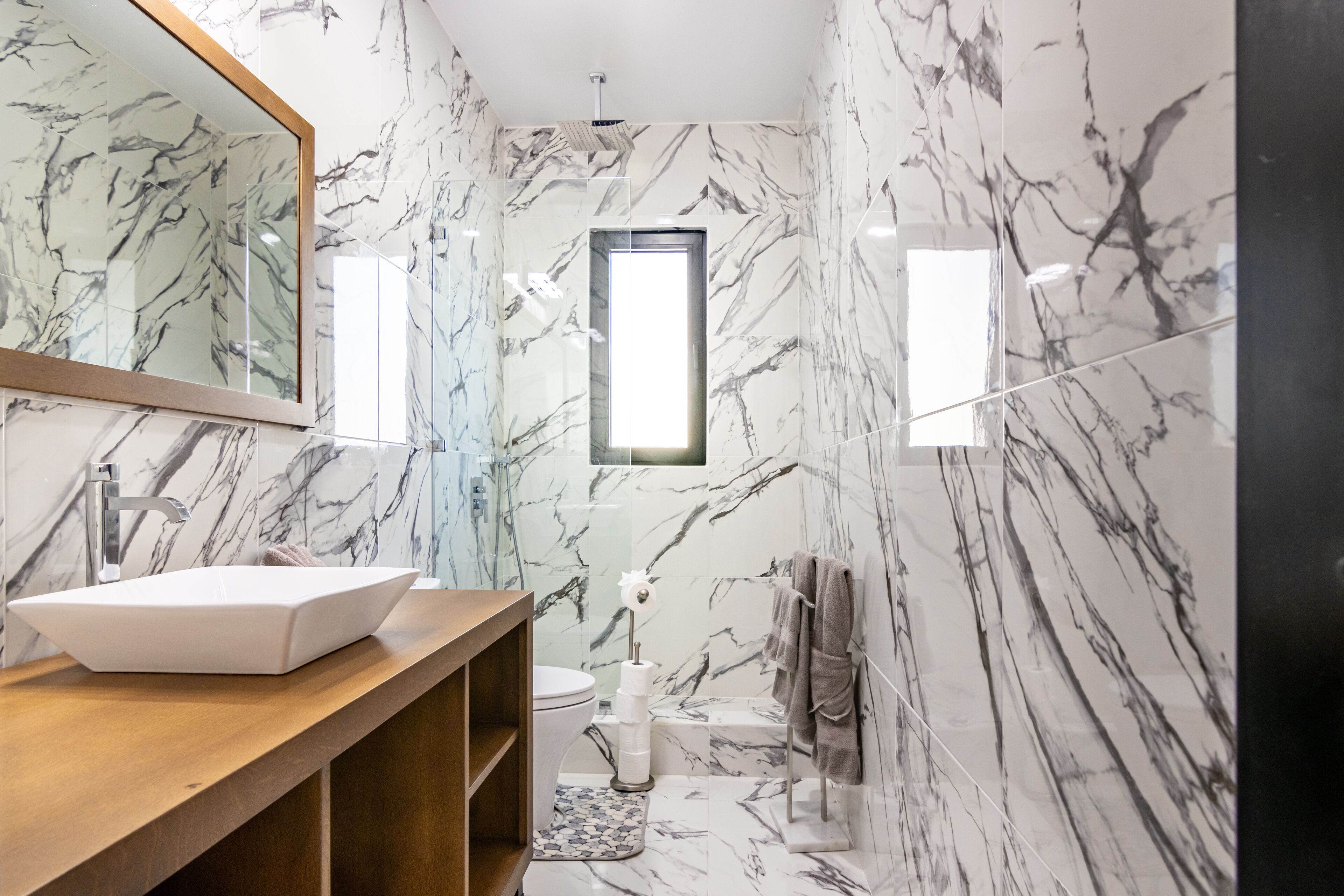 A modern bathroom with a marble backsplash, a wooden vanity, a white sink, and a toilet.