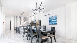 A modern dining area with a marble floor, dark chairs, a central table, and a contemporary chandelier.