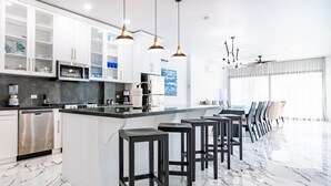 A modern kitchen with white cabinets, a marble countertop, and black stools.