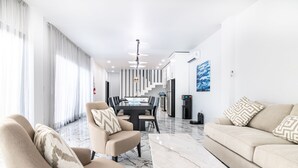 A modern living room with a sofa, armchair, and coffee table, a dining area with a table and chairs, and a staircase leading to an upper floor.
