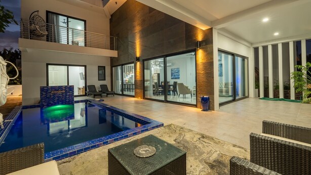 A modern indoor pool area with a glass wall, lounge chairs, and a dining area.