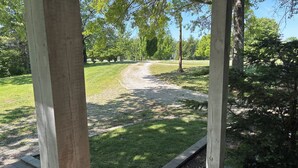 Een overdekt buitengebied met een grindpad dat leidt naar een gazon, omgeven door bomen.