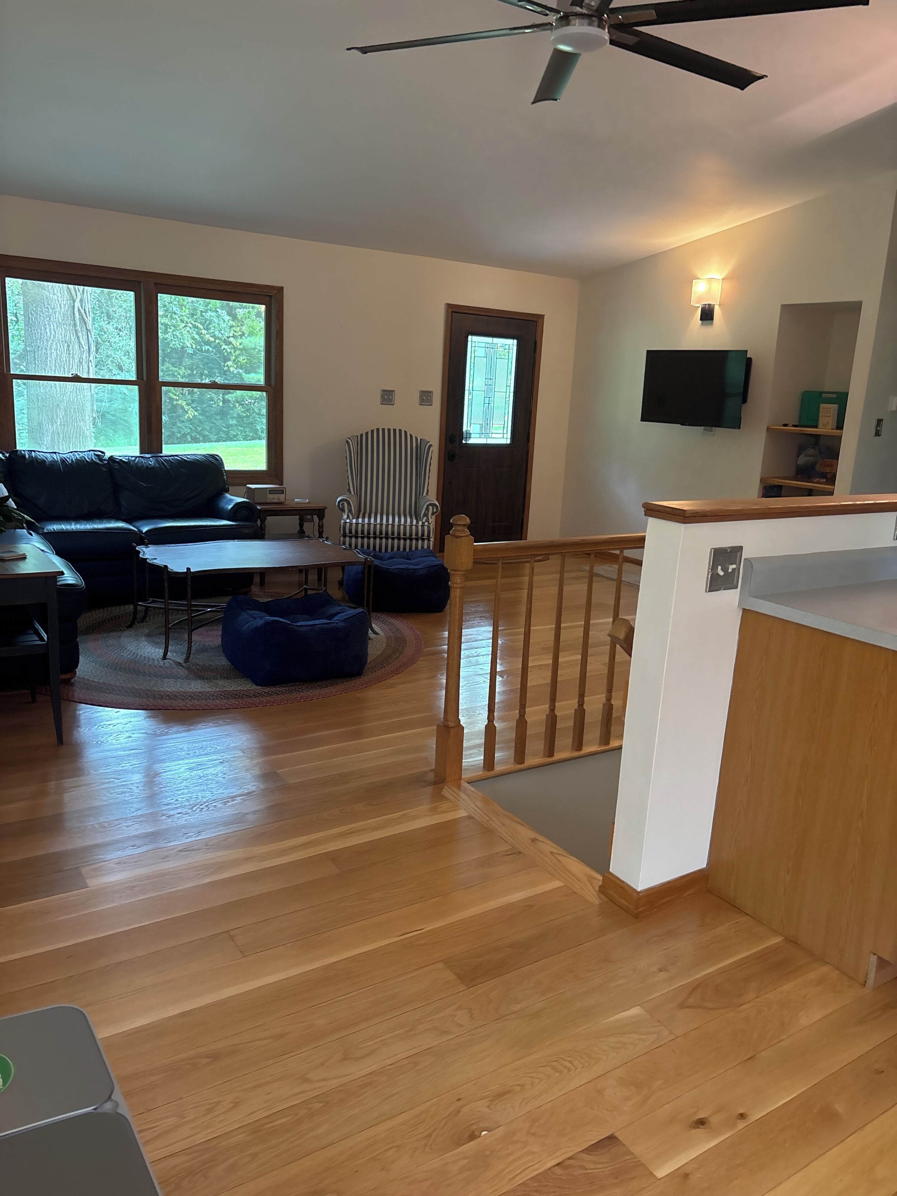 Een ruime woonkamer met een bank, fauteuil en salontafel. Een houten trap met leuning leidt naar een verdieping.