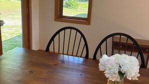 Een eettafel met stoelen, een raam met uitzicht op groen en een vaas met bloemen.